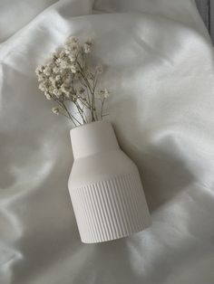 a white vase sitting on top of a bed next to a white sheet with flowers in it