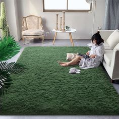 a woman sitting on top of a green rug in a living room next to a couch