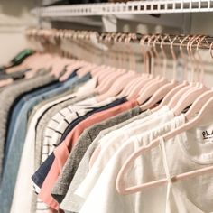 clothes hanging on racks in a closet with white walls and shelves filled with t - shirts