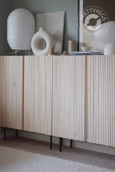 a wooden cabinet sitting on top of a hard wood floor next to a white vase