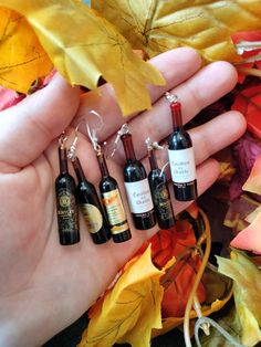 four wine bottles are being held in the palm of someone's hand with autumn leaves around them