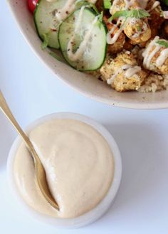 a white bowl filled with salad and dressing next to a small bowl full of vegetables