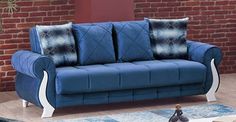 a blue couch sitting in front of a brick wall with pillows on top of it