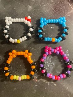 four different colored bracelets sitting on top of a table next to an orange, yellow, and black beaded bracelet