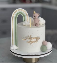 a white cake with a pink teddy bear on top and a rainbow decoration around it