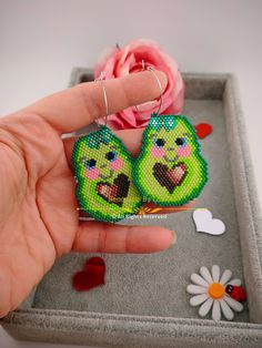 a hand holding two small green birds in front of a pink flower on a gray tray