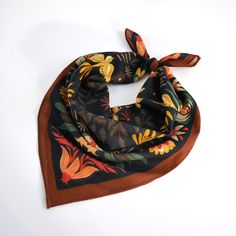 a square scarf with an orange and yellow flower design on it, sitting on a white surface