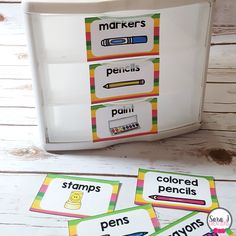 four different colored pencils and markers in front of a white container on a wooden table