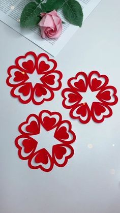 three red paper flowers sitting on top of a white table next to a pink rose