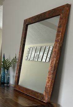 a mirror sitting on top of a wooden table next to a vase with flowers in it