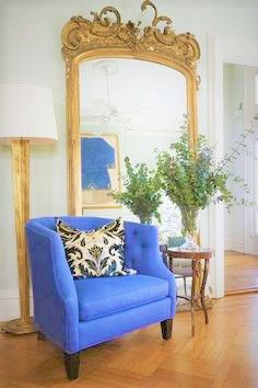 a living room filled with furniture and a large gold framed mirror on the wall above it