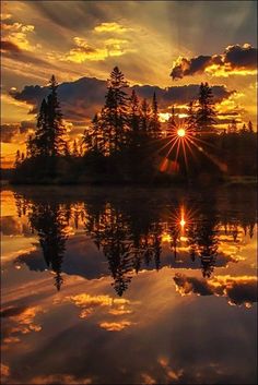 the sun is setting over a lake with trees in it and clouds reflected in the water