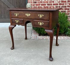 an old wooden desk with gold decorations on the top and bottom drawer, sitting in front of a brick wall