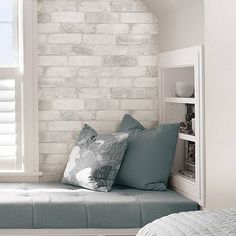 a white brick wall in the corner of a room with a bed and pillows on it