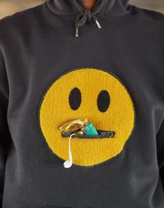 a person wearing a black sweatshirt with a yellow smiley face on it's chest