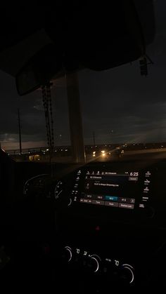 the dashboard of a car at night with lights in the distance and dark clouds overhead