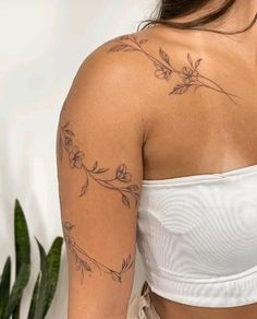 the back of a woman's shoulder with flowers and leaves tattooed on her arm