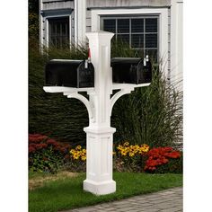 two mailboxes are attached to a white post in front of a house with colorful flowers