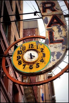 an old neon sign hanging from the side of a building with a clock on it