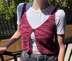 a woman standing next to a fence wearing a red knitted vest