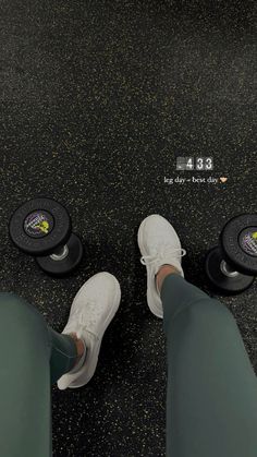 a person with white shoes standing next to two black dumbbells on the ground