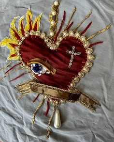 a red heart with gold accents and a cross on the side is surrounded by beads