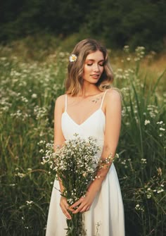 a woman in a white dress holding a bouquet of wildflowers and looking at the camera