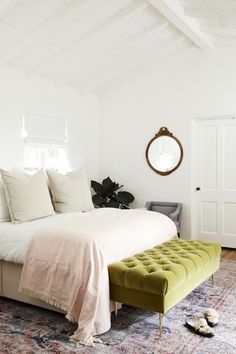 a bedroom with a bed, ottoman and mirror