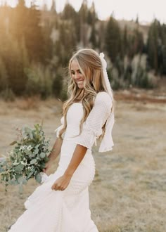 a woman in a white dress holding a bouquet and walking through the grass with her back to the camera