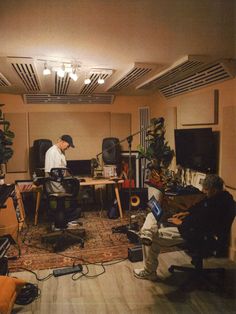 two men sitting at desks in a room with speakers and laptops on the floor