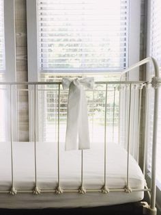 a white crib in front of windows with blinds on both sides and a sheet hanging from the rails