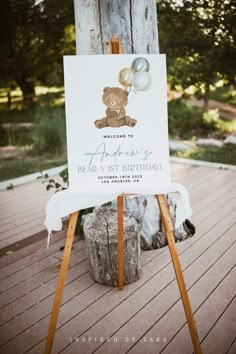 a welcome sign with a teddy bear sitting on it's easel in front of a tree