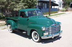 an old green truck is parked on the street