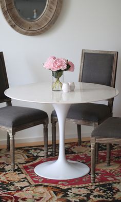 a white table with two chairs and a vase filled with flowers on top of it