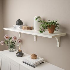 two white shelves with books and vases on them, one shelf is holding flowers