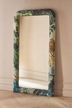 a mirror sitting on top of a hard wood floor next to a wall with a plant painted on it