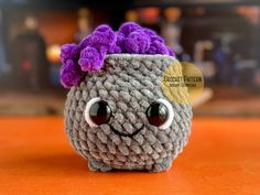 a crocheted toy with purple hair and big eyes on an orange counter top