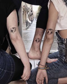 three people sitting on the ground with their legs crossed and one has two small tattoos