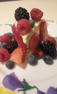 a piece of cake with berries and cream on it sitting on a flowered plate