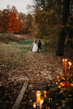 a bride and groom standing in the middle of a forest with candles lit on the ground