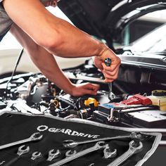 a mechanic working on the hood of a car with wrenches and tools in his hand