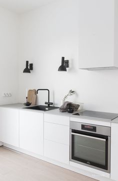 a white kitchen with an oven, sink and stove top on the countertop in front of two black lights