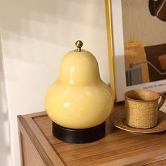 a yellow lamp sitting on top of a wooden table next to a cup and saucer