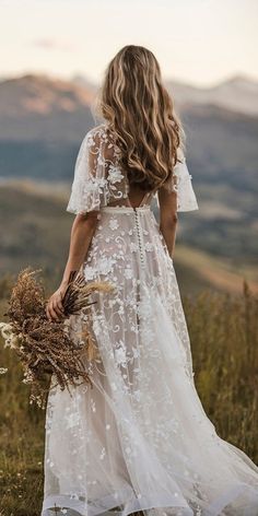 a woman in a white dress is standing on a hill with her back to the camera