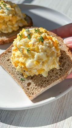 a person is holding up a piece of bread with eggs on it and garnished with herbs