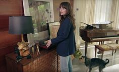 a woman standing next to a piano in a living room with a dog on the floor