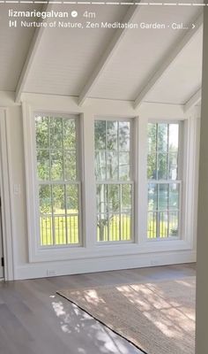 an empty room with three windows and a rug on the floor in front of it