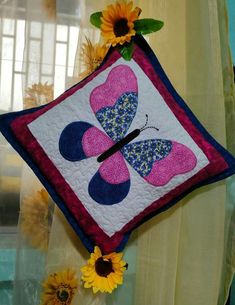 a decorative pillow hanging on the side of a window with sunflowers in front of it