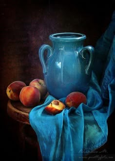 a blue vase sitting on top of a table next to peaches and a blue cloth