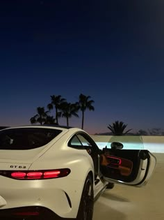 the rear end of a white sports car parked in front of a pool at night